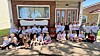 A large group poses outside a brick building in front of a covered entrance and windows.