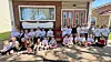 A large group poses outside a brick building in front of a covered entrance and windows.