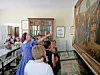 A group of visitors stands in a gallery room looking at a large mural and framed displays.