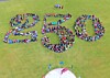 Large group of people arranged to form the number 250 on a grassy field.