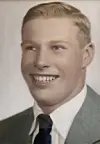 Smiling young man in a suit jacket, white shirt, and dark tie posed against a plain background.