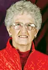 Portrait of an elderly woman wearing glasses and a red jacket against a dark background.