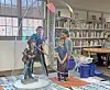 Children stand around a bubble activity station inside a library with bookshelves and tables behind them.