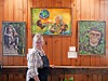 Woman standing in front of a wooden wall with several framed paintings and a small label.