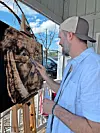 Man painting a large dog portrait on a canvas at an easel outdoors.