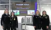 Four students stand indoors beside a digital display that says “THANK YOU!” and “Any Questions?”