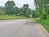 Curved empty road with grass, trees, and utility lines under cloudy skies.