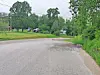 Curved empty road with grass, trees, and utility lines under cloudy skies.