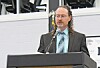 Man speaking at a podium with a microphone in an indoor venue.