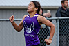 Runner in a purple jersey running past a chain-link fence at an outdoor track meet.