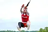 Athlete in red uniform jumping outdoors against a bright sky.