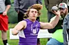 Athlete in purple uniform throws a shot put during an outdoor track and field event.