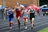 Four runners compete in a track race on an outdoor track.