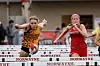 Two runners jump over hurdles during a track race on a track field.