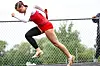 Athlete in red and white uniform jumps over a hurdle on an outdoor track.