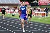 A runner in blue leads other athletes on a track during a race.