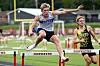 Two athletes jump over hurdles during an outdoor track race.