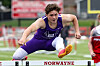 Athlete in purple clears a hurdle on an outdoor track field.
