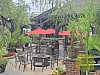 Outdoor restaurant patio with black tables, chairs, red umbrellas, and potted plants.