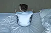 Person seen from above sitting on a bed with hands near their head.