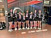 A group of young athletes in matching uniforms stands indoors, holding medals and posing for a photo.