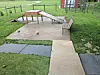 Outdoor dog agility ramp and platform on concrete in a fenced grassy yard.