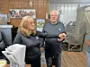 Two people stand in a workshop surrounded by papers, equipment, and wall displays.