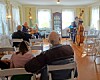 People seated in a room watch musicians play strings near the back wall.