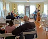 People seated in a room watch musicians play strings near the back wall.