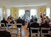 Musicians play in a living room as audience members sit in chairs facing the performers.