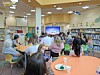 Students seated at tables in a school library watching a presentation on a screen.