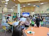 Students seated at tables in a school library watching a presentation on a screen.