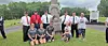 A group poses on grass in front of a stone memorial monument outdoors.