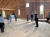 People standing inside an unfinished wooden building with exposed framing and a bare floor.