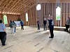 People standing inside an unfinished wooden building with exposed framing and a bare floor.