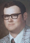 Portrait of a man in glasses wearing a patterned jacket and tie.