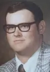 Portrait of a man in glasses wearing a patterned jacket and tie.