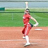 Softball pitcher in red uniform throws a pitch on a dirt field.