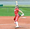Softball pitcher in red uniform throws a pitch on a dirt field.