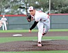 Baseball pitcher in white uniform and red cap throwing a pitch on a field.