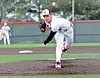 Baseball pitcher in white uniform and red cap throwing a pitch on a field.