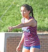 Female athlete in a blue and red uniform gestures outdoors near a track.