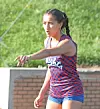 Female athlete in a blue and red uniform gestures outdoors near a track.