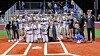 Two youth baseball teams and coaches pose together on a baseball field at night.