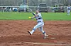 Softball pitcher in white uniform throwing a yellow ball on a dirt field.