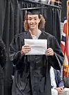 A graduate in cap and gown holds a diploma while standing on stage.
