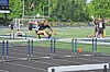 Runner jumps over a hurdle on an outdoor track during a track and field event.