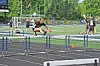 Runner jumps over a hurdle on an outdoor track during a track and field event.