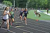 Several runners race on an outdoor track while spectators sit along the edge.