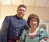 Two people standing indoors, wearing historical-style costumes and facing the camera.